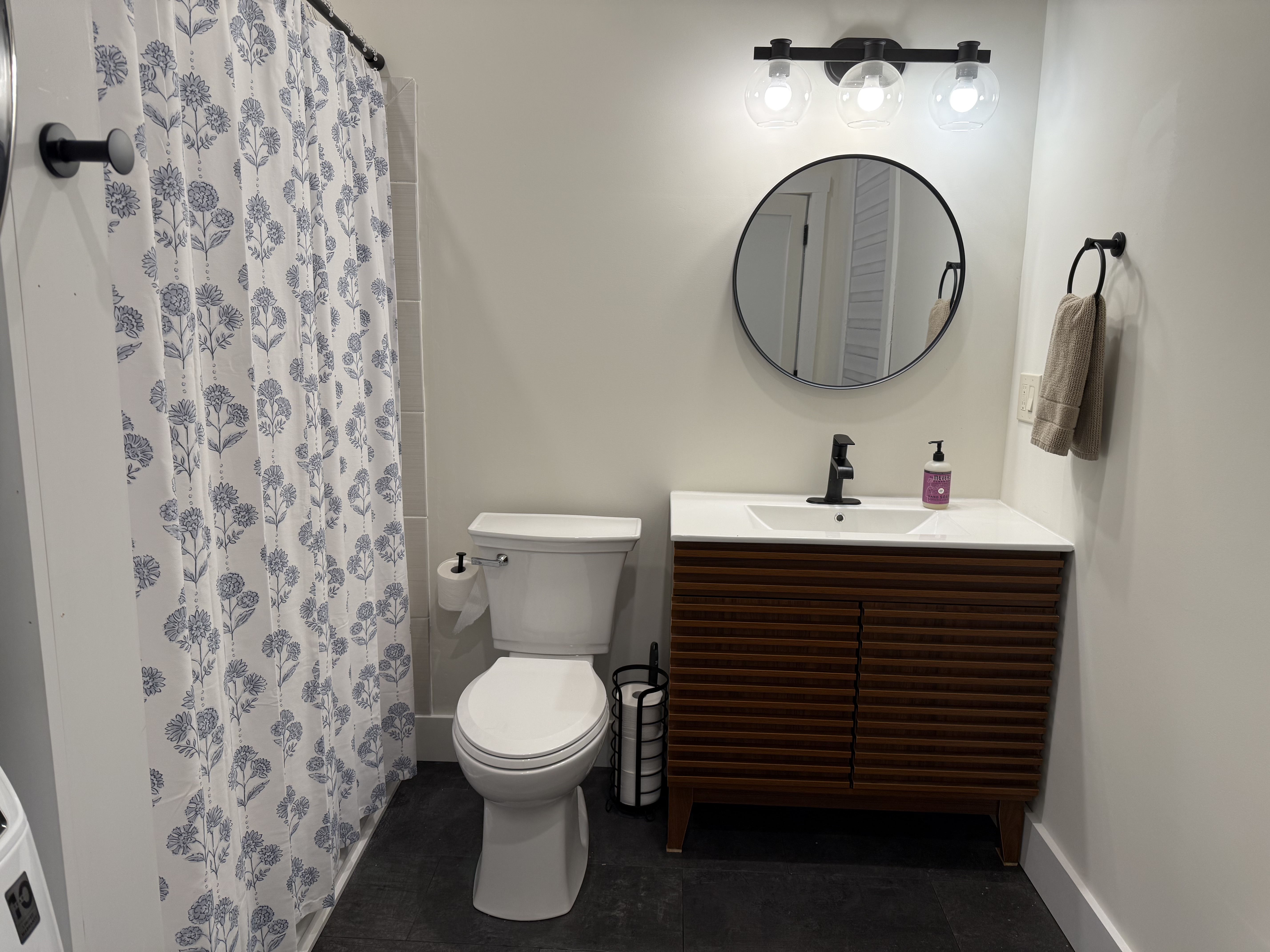 Full bathroom with floral shower curtain and wood slat vanity